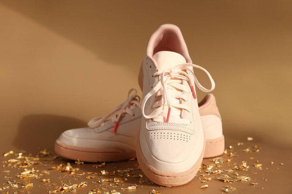 Unbranded beige sneakers and pieces of gold paper firecracker on golden background, new Year party. Front view, mockup.
