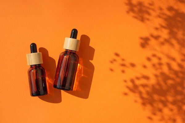 Amber glass dropper bottles different sizes with bamboo lid on an orange background. Top view with plant shadow.