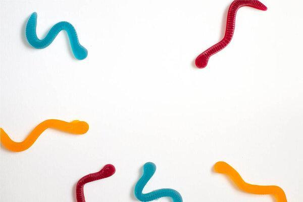 jelly fruit candies of different colors in the form of worms on a white paper background. Imitation of crawling candy on paper