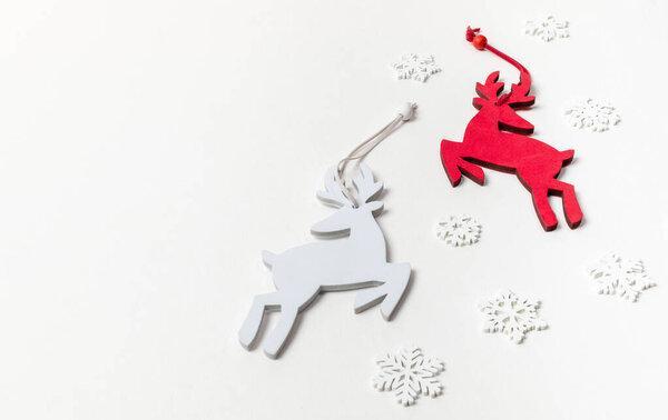 Festive Christmas background with Xmas decorations: two deer red and white and white wooden snowflakes on white backdrop. Top view, flat lay. Copy space for text.