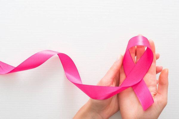 Symbol of Breast Cancer Awareness Month in October. Female hands holding pink breast cancer awareness ribbon over white background. Women's healthcare and medicine concept