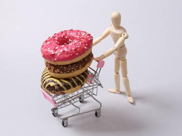 Puppet rolls a mini shopping cart with a stack of donuts on white background