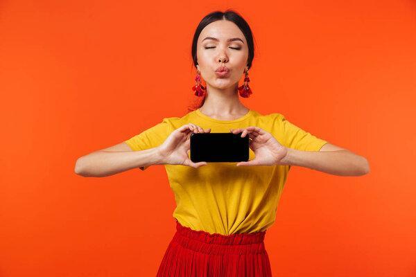 Excited happy young woman posing isolated over orange wall background showing display of mobile phone.