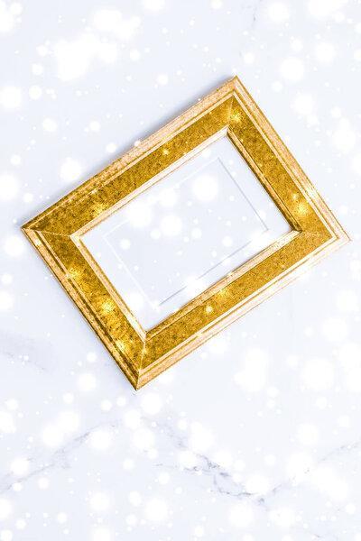Golden photo frame and glowing glitter snow on marble flatlay ba