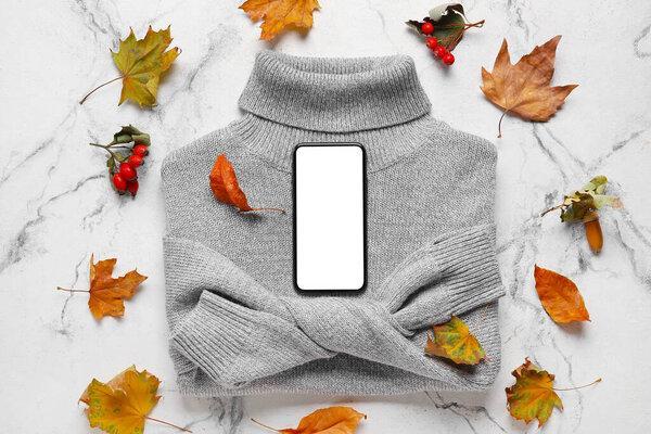 Female sweater, autumn leaves, rowan and mobile phone on light background. Black Friday sale