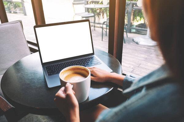 Mockup image of a woman using and touching on laptop touchpad with blank white desktop screen with coffee cup on the table 