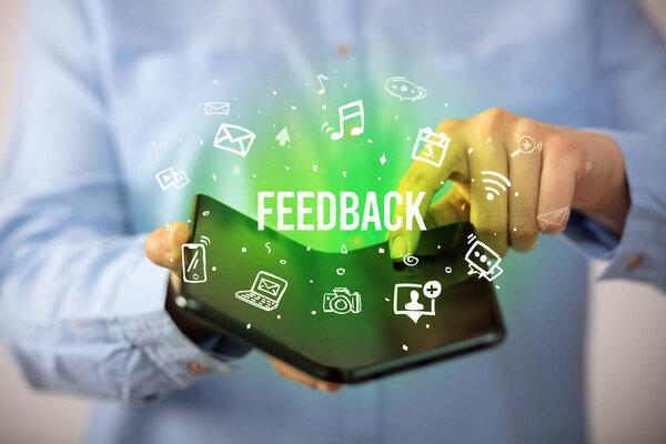 Businessman holding a foldable smartphone with FEEDBACK inscription, social media concept
