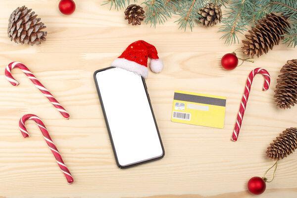 Mockup blank white screen smartphone and credit card on white wooden desk background for Christmas and New Year. Cristmas online shopping concept. Top view.