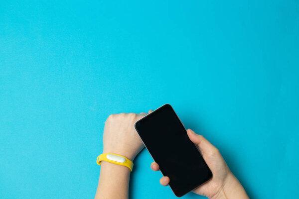 Female hands with tracker and smart phone on blue background. Flat lay, top view
