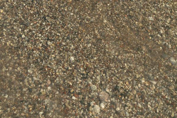Sea waves on pebble beach texture background. Transparent ocean water, rocky shore pattern, summer mockup with copy space, stone shoreline, vacation concept