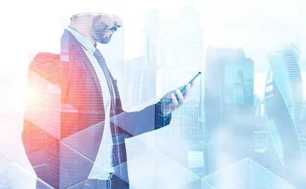 Side view of unrecognizable bearded businessman looking at his smartphone screen standing over cityscape background with double exposure of triangular patterns. Toned image