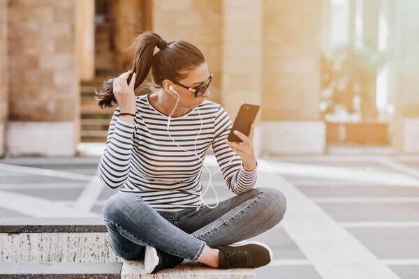 A young happy teen girl using a smart phone sititng in the city