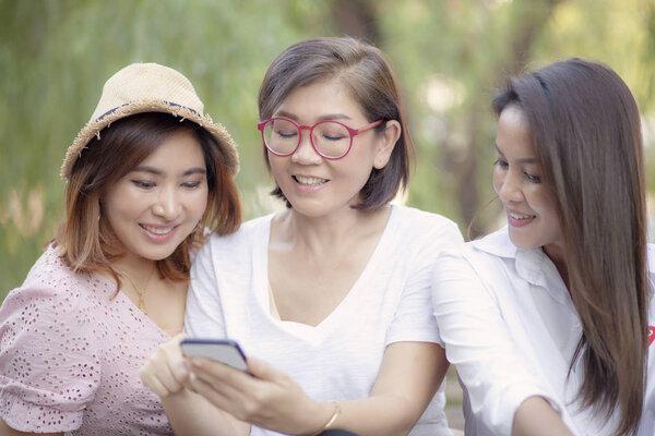 three asian woman looking on mobile phone screen with toothy smiling face 