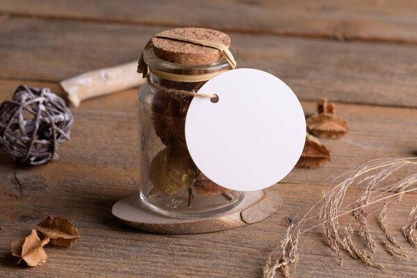 Round white tag mockup on glass jar with dry perfume a wooden background with boho decoration, element for packing. Label product mockup and natural eco design. Bohemian wedding gift, wedding favors