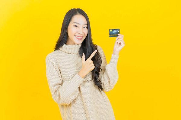 肖像美丽的年轻亚洲女人微笑与信用卡在彩色背景