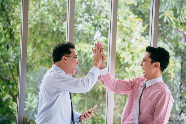 Success Businessman happy got good news from mobile smart phone that business so success. Asian young business man raise hand with happiness, smiling, excited after got great news from phone.