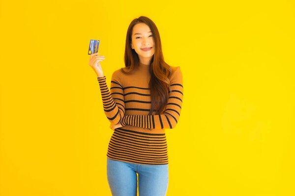 形象漂亮的年轻亚洲女人用智能手机或带信用卡的手机在孤立的黄色背景下进行网上购物