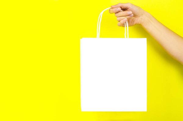 White paper bag in a female hand on a yellow background