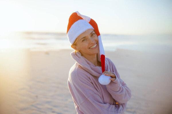 happy modern woman in cosy sweater with striped christmas hat at the beach in the evening.