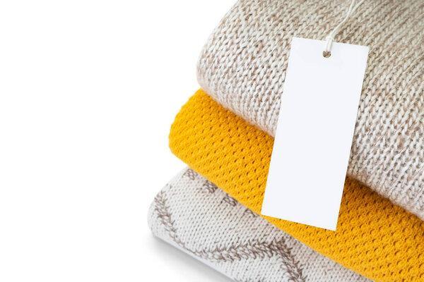 White blank rectangular clothing tag on stack of knitted clothes isolated on white background