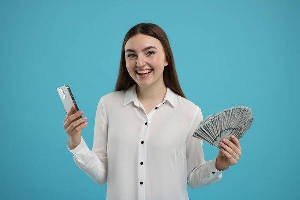 快乐的女人，带着美元钞票和浅蓝色背景的智能手机
