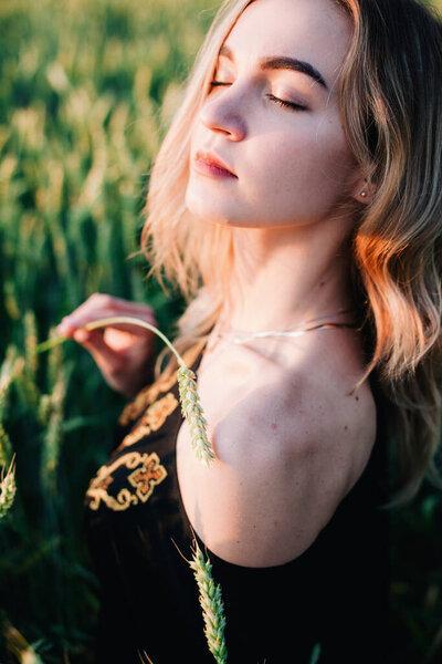 Young, slender girl embroidered dress in a large wheat field at sunset