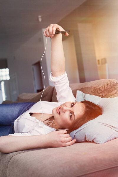 Cheerful brunette young woman in white shirt making self image lying on the sofa in living room. Vertical