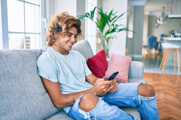 Young hispanic man smiling happy using smartphone at home