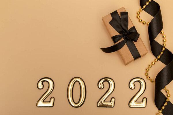 New Year 2022. Top view New Year mockup on beige background: black ribbon, gift box, golden numbers and multicolored sparkles. Layout of postcards, invitations.