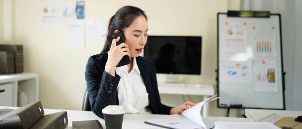 businesswoman talking on smartphone and reading document, solving corporate business problem. Female employee discussing document by cellphone, receive news..