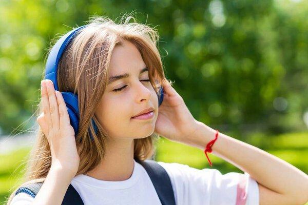 caucasian girl teenager student listening to the music stereo favorite song in headphones outdoors in city park.