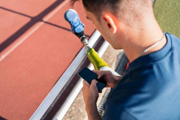 Disabled man athlete using his phone in the stadium.