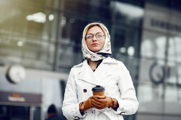 Young stylish pretty woman posing in the city streets and using 