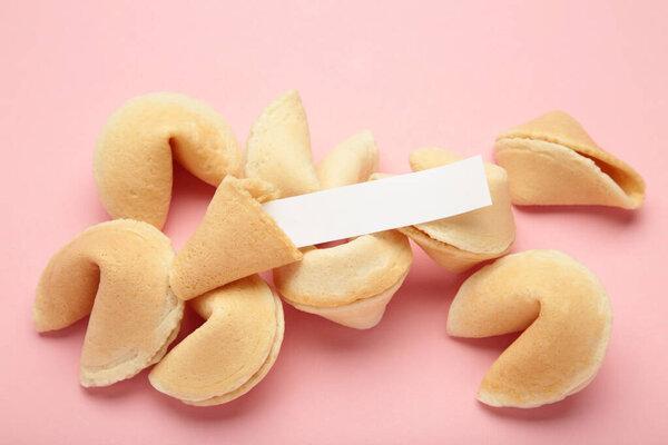 Tasty fortune cookies and paper with prediction on pink background.