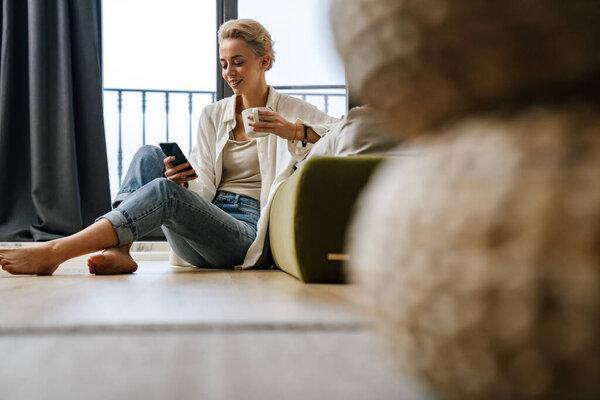 Woman relaxing while leaning on a sofa, using smartphone at home