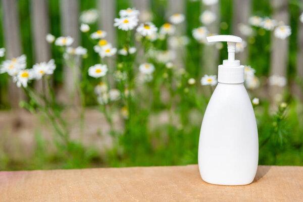 white cosmetic bottle for soap or shampoo on wooden shelf with chamomile background. For montage of your product