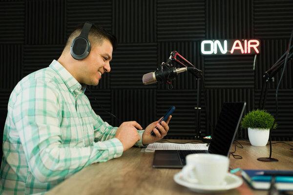 Latin broadcaster smiling while reading messages on social media on air while on his talk show on the radio 