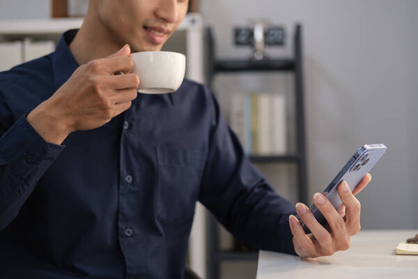 Young businessman drinking coffee and reading massage on mobile phone.
