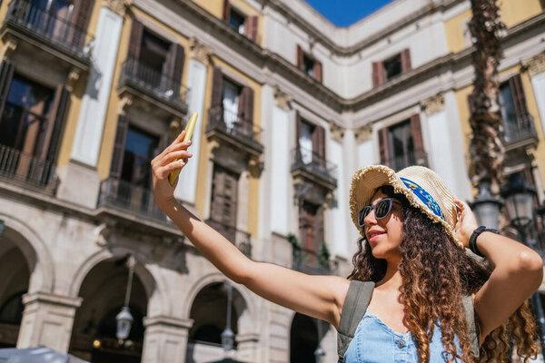 young turkish female traveler wearing a straw hat and sunglasses taking a selfie at city square
