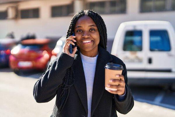 African american woman talking on smartphone drinking coffee at street