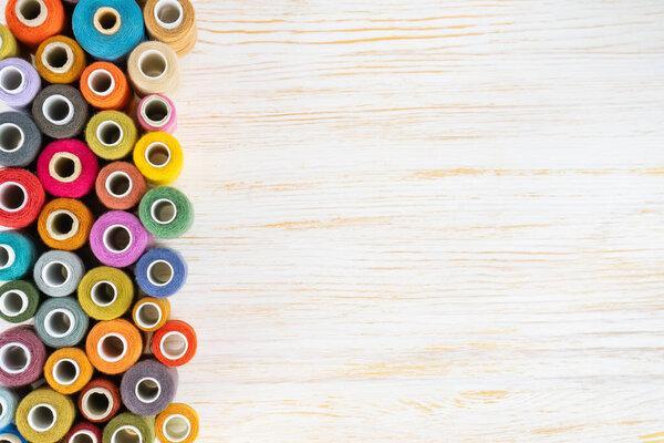 Sewing thread spools multicolored background, scattering of various colors sewing threads, colored yarns on white wooden surface with copy space. Flat lay, top view, mockup, template