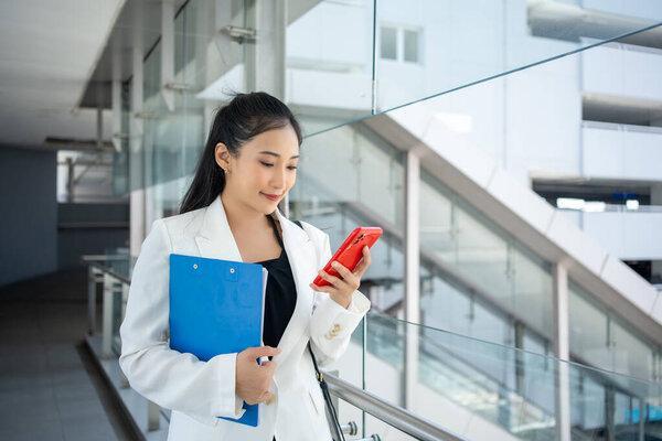 Young businesswoman holding document and using a smartphone while walking through the city