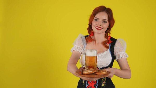 Medium yellow background isolated shot of a young German woman, waitress wearing a traditional costume, holding a platter with pretzels, wurst and a glass of beer. Octoberfest, breasts, advertisement.