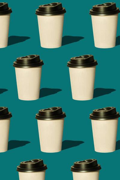 Coffee to go regular pattern made of photo on a turquoise background. Kraft paper cups with black lids and natural bright sun shadows. Lifestyle take away hot drinks concept. Trendy flatlay, top view.