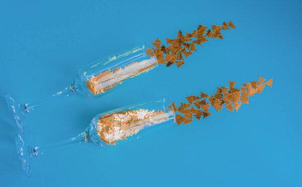 Two champagne glasses with shiny bright confetti on a blue background. Invitation to a party. The concept of Christmas celebration.