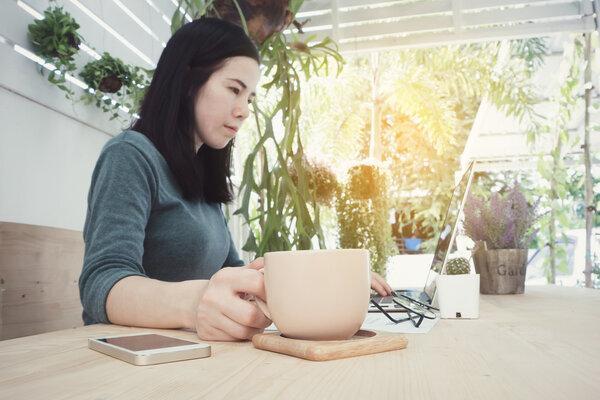 Office table with Asian woman watching on laptop and drink coffe