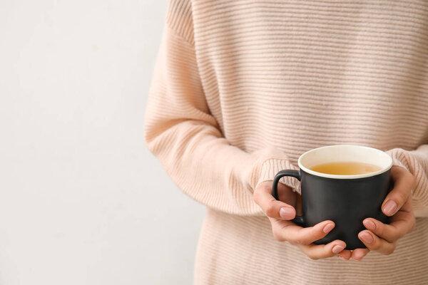 Woman with cup of hot tea on light background