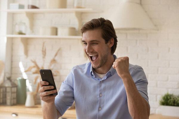 Overjoyed young male raise clenched fist looking on phone screen
