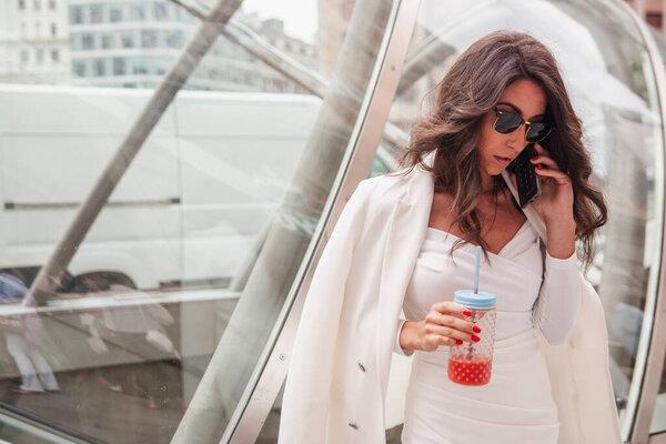 YOUNG URBAN GIRL WITH A JUICE IN THE CITY WITH MOBILE PHONE CONSULTING