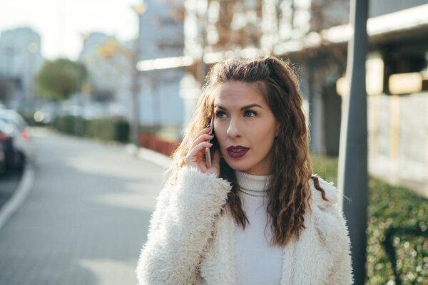 Portrait of beautiful young woman talking on the mobile phone at street